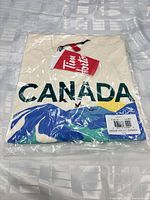 Front view of sealed Tim Hortons CANADA T-shirt showing graphic through plastic