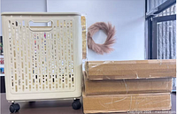 Assembled beige plastic laundry basket on wheels beside three sealed boxes