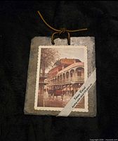 Front of slate plaque showing printed New Orleans street scene, leather hanging cord and packaging band