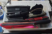 Tray containing assorted black wallets, red pouches, pens, drawstring pouch, eyeglass sleeve