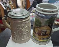 Front view of both steins showing relief stein with pewter lid and Bucks County scene stein