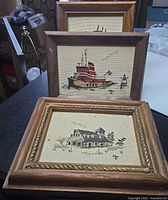 Three framed cross-stitch pieces stacked showing front views