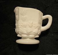 Profile view showing handle, embossed grape motif and pedestal foot