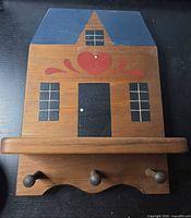 Front view showing house shape, shelf, three hooks, painted design