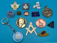 Group shot of fourteen Masonic related pins, medallions, keychain on blue background