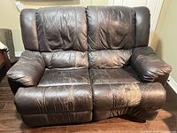 Front view of dark brown two-seat bonded leather reclining loveseat showing overall style and wear