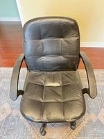 Front view of black faux leather office chair showing seat, backrest and armrests, wear and tears visible