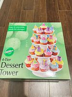 Front of box showing assembled 4-tier dessert tower loaded with cupcakes