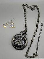 Front view of gunmetal pocket watch with chain and pair of enamel Donald Duck earrings