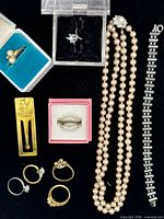 Overview of all jewelry items laid out: seven rings, pearl necklace, silver-tone bracelet, gold-tone bookmark
