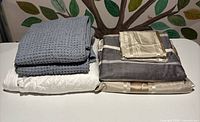 Stack of grey crochet blanket, white duvet cover, grey/beige striped duvet cover set with beige pillow shams