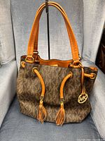 Front view of Michael Kors brown monogram shoulder bag with tan leather handles and tassels