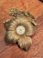 Front view of brushed gold-tone flower pendant watch with chain