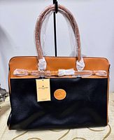 Front view of tote showing black body, tan trim, handles, logo patch, hang tag