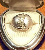 Ring front view in display box showing brushed silver dome and rhinestone band