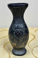 Full view of black pottery vase showing floral engraving and pedestal foot