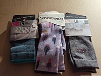 Front of three unopened sock packages showing Smartwool and Icebreaker branding