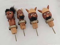 Front view of four teak stoppers showing heads, corks, metal spouts