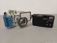Front view of Canon waterproof case with blue latch next to Canon Snappy EL camera