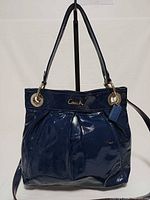 Front view of Coach navy patent pleated hobo bag showing logo, pleats, hangtag