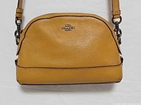 Front view of caramel Coach dome crossbody bag showing logo, leather texture, hardware