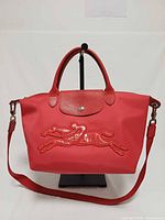 Front view of red Longchamp Neo Victoire handbag on stand showing horse applique, handles and strap