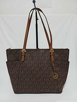 Front view of brown MK monogram tote with straps and charm displayed