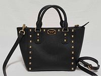 Front view of black saffiano leather Michael Kors Sandrine Stud satchel with gold studs and detachable strap attached