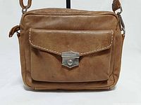 Front view showing flap pocket with twist-lock, leather texture, stitching