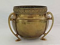Front view of brass planter showing three handles, decorative rim and feet