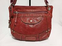 Front view showing cranberry leather, front flap pocket, zip pocket, key charm, Fossil logo patch