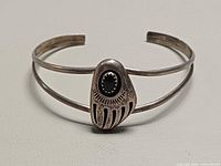 Front view of sterling silver split-shank cuff with bear paw motif and dark stone