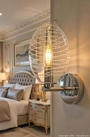 Wall sconce installed in bedroom setting showing polished metal backplate and oval ribbed glass shade illuminated