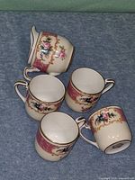 Four demitasse cups and one creamer showing pattern and gold trim