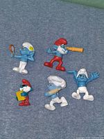All five Smurf figurines laid out on grey surface