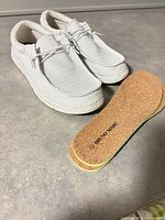 Pair of white Bruno Marc slip-on sneakers with extra cork insoles shown