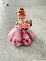Front view of pink-dressed girl figurine holding flower basket