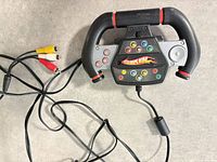Front view of steering wheel controller showing buttons, Hot Wheels logo and attached AV cable