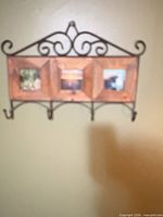 Full view of wall coat rack showing wood frame, metal scroll top, four hooks, three photo openings
