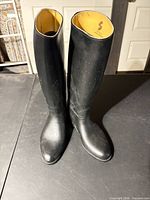 Full view of both black knee-high boots standing upright on table