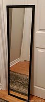 Front view of black framed full-length mirror leaning on wall