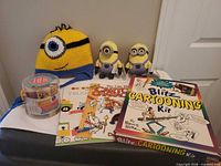 Group shot showing both Minion plushes, crochet hat, Blitz Cartooning Kit, two drawing books, stamp set