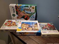All four boxed items: Clementoni puzzle mat, Ravensburger 300-pc puzzle, two Bits & Pieces puzzles
