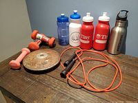 Group shot of discus, dumbbells, jump rope, five water bottles on table