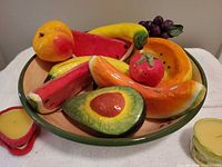 Overall view of papier-mâché fruits arranged in ceramic bowl with two candles visible
