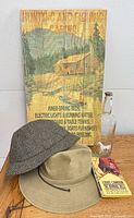 Group shot of wood sign, two hats, glass bottle and paperback book