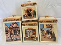 Front view of four stacked ceramic canisters showing different Hummel scenes