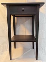 Front view of black engineered wood end table with drawer and shelf
