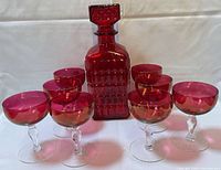 Ruby red decanter with stopper flanked by eight stemmed glasses