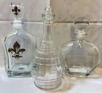 Front view of three clear glass decanters showing shapes and stoppers